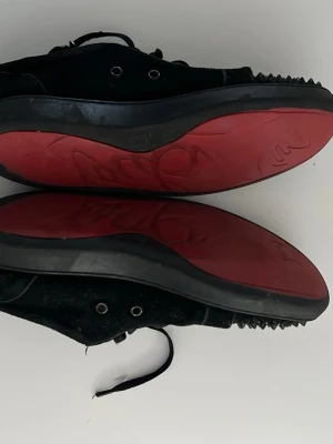Svarta skor med spikar röd sula - Unika svarta sneakers i mocka som liknar  Christian Louboutin med coola svarta nitar på tån och klassisk röd sula. Skorna har snörning och rund tå, samt en lyxig känsla med skinnfoder. Perfekta för dig som vill sticka ut med edgy detaljer. Inte äkta loubs 