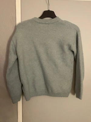 Ljusblå stickad tröja - Mysig ljusblå stickad tröja med rund hals och ribbade muddar vid ärmslut och nederkant. Perfekt för att hålla värmen under kyliga dagar. Enkel och stilren design som passar till många olika outfits.