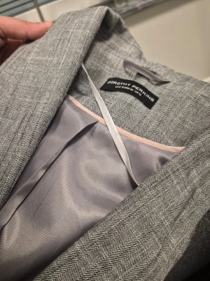 Grå kavaj från Dorothy Perkins  12 40 M - Snygg grå kavaj från Dorothy Perkins med diskret fiskbensmönster. Kavajen har en klassisk passform, en knapp framtill och två fickor. Fodrad med ljusgrått tyg för extra komfort. Perfekt för en stilren och modern look.