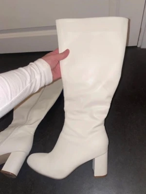 Vita stövlar - Säljer ett par vita knähöga stövlar med bred klack och rund tå. Stövlarna har dragkedja på insidan och är gjorda i ett slätt, glansigt material som liknar skinn. Perfekta för att lyfta vilken outfit som helst. vita stövlar som är använda endast 1 gång, storlek 40, jätte varma och bekväma att gå i. Pris kan diskuteras vid snabb affär.