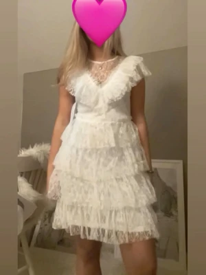 Vit spetsklänning från Bubbleroom - Supersöt vit spetsklänning från Bubbleroom med volangdetaljer och flera lager. Klänningen har v-ringad spets upptill, kort ärm med volang och knappar i ryggen. Perfekt för sommarens alla tillfällen! Studentklänning som endast är använd 1 gång