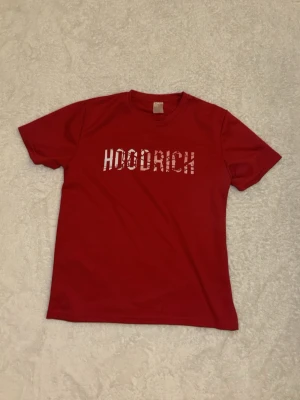 Röd HOODRICH t-shirt med tryck - Snygg röd t-shirt från HOODRICH med ett vitt grafiskt tryck på bröstet. T-shirten har klassisk passform, rund halsringning och korta ärmar. Perfekt för dig som gillar streetwear och vill sticka ut med ett coolt statement-plagg.