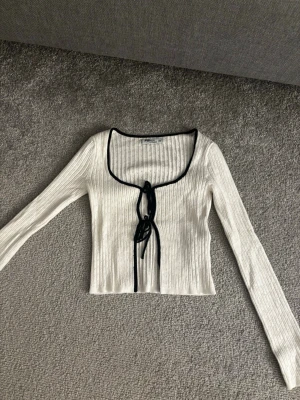 vit ribbad topp med knytning - en vit ribbad långärmad topp med svart knytning och u ringning, den är aldrig använd🩷kontakta för fler bilder eller frågor!