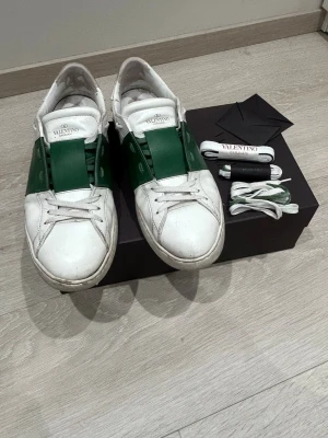 Valentino vita och gröna sneakers - Snygga sneakers från Valentino i vitt läder med gröna detaljer över sidorna och tungan. Klassisk låg modell. Allt på bilden medföljer. Rätt slitna på insidan men det ser man inte när man har på sig dom. 