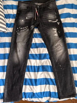 Dsquared2 jeans - Säljer ett par svarta jeans från Represent med slitna detaljer, färgstänk och dragkedja framtill. Jeansen har raka ben och klassisk femficksmodell. Materialet är denim i bomull och de har en cool, streetinspirerad look. Storlek 50 vilket motsvarar L.  W 34-35. Passar också M.