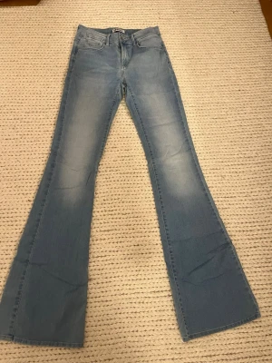 Långa ljusblå bootcut jeans från ONLY - Säljer ett par ljusblå bootcut jeans från ONLY med klassisk femficksmodell. Jeansen har en snygg tvätt och vida ben som ger en retrovibe. Perfekta för dig som gillar en avslappnad men trendig stil. Innerbenslängd ca 88cm