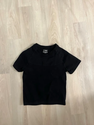 Svart träningstshirt - En svart t-shirt med ribbade detaljer runt halsen och axlarna. T-shirten har korta ärmar och en klassisk rund halsringning. Perfekt basplagg som funkar till allt och är gjord i mjuk bomull.