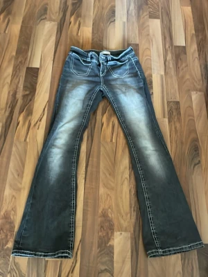 Gråa bootcut jeans från ginatricot - Snygga gråa bootcut jeans från Gina med markerade vita sömmar och dubbla knappar i midjan. Jeansen har en lätt tvättad look och klassiska fickor fram och bak. Perfekta för en trendig och avslappnad stil.