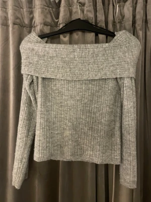 Grå off shoulder stickad tröja Divided - Trendig grå stickad tröja från H&M Divided med bred off shoulder-krage och ribbad struktur. Långärmad modell i mjukt material som passar perfekt till jeans eller kjol. Enkel att styla för en avslappnad men snygg look.