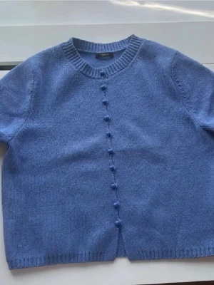 Blå stickad kortärmad kofta - En snygg blå stickad kofta med korta ärmar, rund hals och blåa knappar från Massimo dutti. Tröjan är i nytt skick då den använts fåtal gånger!