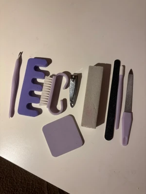 Lila manikyrset med nagelverktyg - Komplett manikyrset i lila och vitt med nagelklippare, nagelfil, polerblock, nagelborste, tåseparatorer, nagelbandsverktyg och buffert. Perfekt för att fixa naglarna hemma med stilrena och praktiska verktyg i plast och metall. ❤️