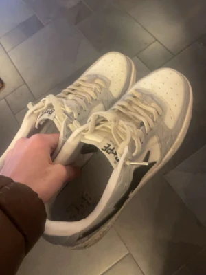 Bape Sta vita sneakers med svart stjärna - Säljer ett par vita Bape Sta sneakers med svart stjärndesign på sidan. Skorna har klassisk låg siluett, vita snören och detaljer i läder. Perfekta för dig som gillar streetwear och vill sticka ut med en ikonisk modell.