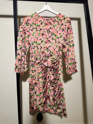 Blommig kortklänning från Zara - Färgglad kortklänning från Zara med blommigt mönster i rosa, grönt, gult och svart. Klänningen har trekvartsärmar, rynkade detaljer och knyt i midjan. Perfekt för dig som gillar att sticka ut med en feminin och lekfull stil.