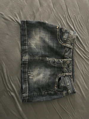 Mörk jeanskjol med slitningar - Cool mörkblå jeanskjol med slitna detaljer och klassiska fickor både fram och bak. Kjolen har en kort modell och stängs med knapp och dragkedja framtill. Perfekt för dig som gillar en avslappnad och trendig stil. Finns ingen lapp så har ingen aning om vilken märke den är. Jag vet inte heller riktigt vad storleken är men den är riktigt liten så ungefär xxs 