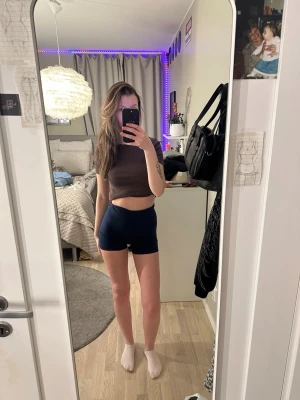 Mörkblå högmidjade tränings shorts  - Säljer ett par mörkblå högmidjade shorts med tight passform. De är gjorda i ett stretchigt syntetmaterial och har snygg scrunch-detalj bak som framhäver formen. Perfekta för träning eller chill dagar.