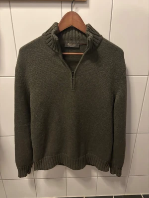 Loro Piana - Säljer en olivgrön stickad tröja från Loro Piana med halvzip och hög krage. Tröjan har ribbstickade muddar vid ärmslut och nederkant, samt en grovstickad känsla som ger en avslappnad look. Perfekt för lager på lager under kyliga dagar. 100% baby cashmere, som ny.