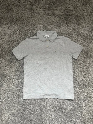 Grå pikétröja från Lacoste - Klassisk grå pikétröja från Lacoste i storlek 176≈Xs och säljs för 200kr!