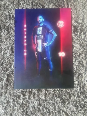 PSG Neymar Jr affischbok - Cool tavla med Neymar Jr i PSG-tröja, med klubbens logga och nummer 10. Snyggt tryck i blått, rött och svart med sportigt tema. Perfekt för fotbollsälskare och samlare av sportmemorabilia.