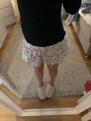 Vit blommig volangkjol - Supersöt kort kjol i vitt med små blommor i rosa och lila toner. Kjolen har flera volanger och är enkel att matcha med olika toppar🌸