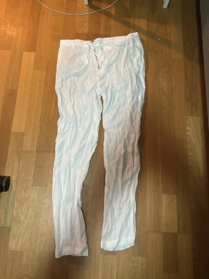 Vita linnebyxor från Zara - Säljer ett par vita linnebyxor med dragsko i midjan och raka ben. Byxorna har en avslappnad passform och är tillverkade i ett lätt och luftigt linnetyg, perfekta för varma dagar. Klassisk design utan synligt märke.