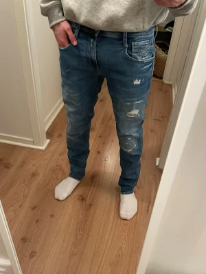 Blå slitna Replay jeans - Säljer ett par blå Replay jeans med slitna detaljer på framsida. Jeansen har klassisk femficksmodell, normal midja och är gjorda i denim. Perfekta för en avslappnad och trendig look.