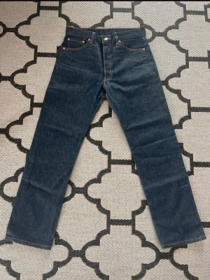 Mörkblå raka jeans från Levi's 501 - Klassiska mörkblå jeans från Levi's med rak passform och fem fickor. Jeansen har kontrastsömmar och en ikonisk läderpatch bak i midjan. Tillverkade i slitstark denim som ger en tidlös look. 501