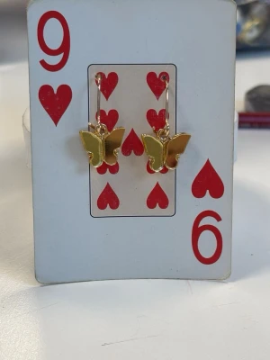 Örhängen med guldfärgade fjärilar  - Säljer ett par gulfärgade örhängen med fjärilar på.    Fjärilarna är i en matt guldfärg och sitter på metallkrokar som också är guldfärgade. Perfekt för dig som vill få en känsla av våren. 