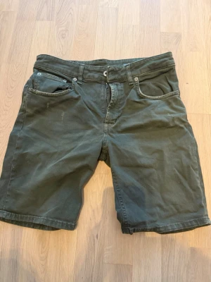 Mörkgröna shorts i bomull - Säljer ett par mörkgröna shorts med klassisk femficksdesign och bälteshällor. De har normal passform och är tillverkade i mjuk bomull, perfekta för varma dagar. Stängs med knapp och dragkedja framtill.
