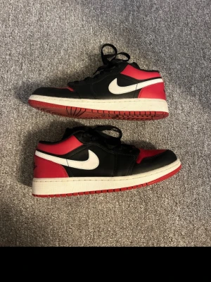 Nike Air Jordan 1 Low svart/röd/vit - Säljer ett par Nike Air Jordan 1 Low sneakers i svart, rött och vitt läder. Perfekta för dig som gillar färgade  sneakers.