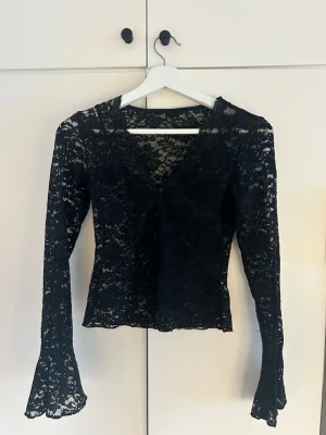 Svart spetsblus med v-ringning - Snygg svart blus i spets med v-ringad hals och långärmad.