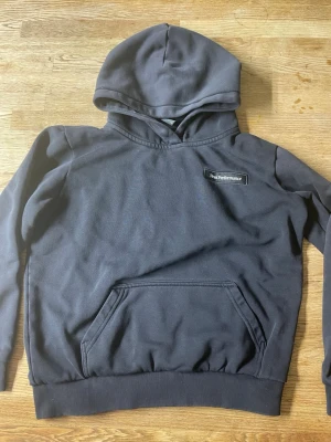Mörkgrå Peak Performance hoodie - Storlek 160. Snygg mörkgrå hoodie från Peak Performance med klassisk känguruficka och ribbade muddar. Märkets logga sitter broderad på bröstet. Tillverkad i mjukt bomullsmaterial och har en stor huva för extra chill vibe.
