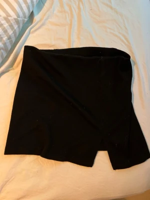 Svart kortkjol med slits - Enkel svart kortkjol med rak passform och en liten slits framtill. Kjolen är stilren och lätt att matcha till olika outfits. Perfekt för dig som gillar minimalistisk stil.