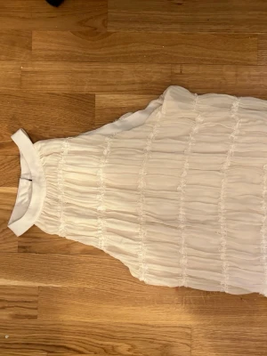 Vit ärmlös blus med volang - Säljer en söt vit blus med hög krage och volangdetaljer. Tror den var köpt i storlek L/M men passar helt klart storlek S.