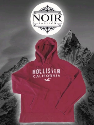 Vinröd hoodie från Hollister - Snygg vinröd hoodie från Hollister med stor vit text 'Hollister California' och logga på bröstet. Klassisk huva med dragsko och magficka framtill. Perfekt för en avslappnad och trendig stil.