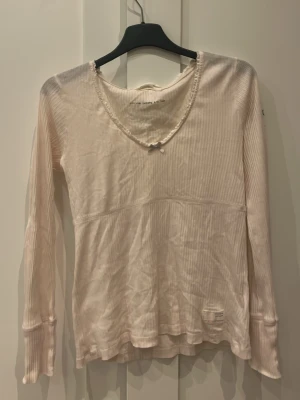 Ljusrosa blus från Odd Molly med tryck - Supersnygg ljusrosa blus från Odd Molly med ett färgglatt tryck i form av ett hjärta och banderoll. Blusen är tillverkad i ett tunt, ribbat material som känns luftigt och skönt. Perfekt för dig som gillar detaljer och unik design.