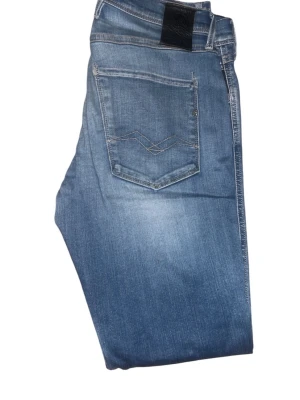 Blå slim fit jeans från Replay - Snygga blå slim fit jeans från Replay med slitningar och ljusa tvättade partier. Klassisk femficksmodell med dragkedja och knapp. Jeansen har en modern passform och är tillverkade i stretchigt denimtyg för extra komfort.