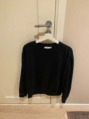 Svart sweatshirt från Weekday - En stilren svart sweatshirt från Weekday med rund halsringning och långa ärmar. Tröjan har en enkel och avslappnad passform, perfekt för en sopig streetwear-look. Tillverkad i mjukt material som känns skönt mot huden.