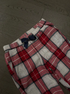 Rutiga pyjamasbyxor med rosett - Mysiga pyjamasbyxor i rött, vitt och mörkblått rutmönster. Byxorna har en mörkblå rosett i midjan och resår vid bensluten för extra komfort. Perfekta för chillkvällar hemma.✨storlek 146/152
