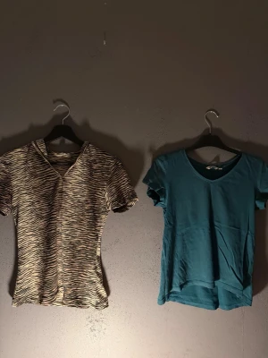 Två t-shirts, zebra och turkos - Säljer två t-shirts: en med zebramönster i beige och svart med v-ringning och en turkos t-shirt med enkel design och v-ringad hals. Båda har korta ärmar och är perfekta för en avslappnad stil.