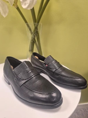 Gorena svarta loafers i präglat läder 42 - Snygga svarta loafers med präglat mönster i lädret och klassisk penny strap över vristen. Skorna har en elegant, smal siluett och låg klack. Perfekta för dig som vill ha en stilren och modern look. Passar till både jeans och kostym.