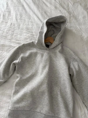 Ljusgrå hoodie från Gina Tricot - Snygg ljusgrå hoodie från Gina Tricot i mjukt sweatshirtmaterial. Klassisk modell med huva och ribbade muddar vid ärmslut och nederkant. Perfekt för en chill och avslappnad stil.