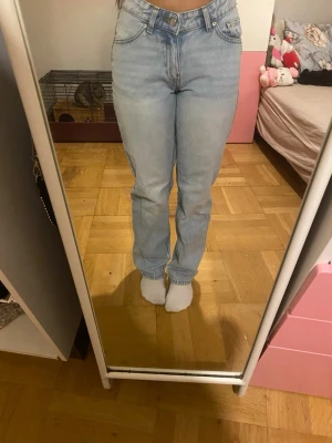 Ljusblå raka jeans med låg midja - Säljer ett par ljusblå jeans med rak passform och låg midja. Klassisk femficksmodell med knapp och dragkedja framtill. Jeansen har en avslappnad look och är tillverkade i denim, perfekta för en trendig vardagsstil.