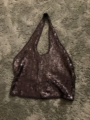 Svart glittrig halterneck topp - Snygg svart halterneck topp med paljetter som ger ett glittrigt intryck. Toppen är ärmlös och har en djup urringning framtill samt dragkedja i ryggen. Perfekt för dig som vill sticka ut med en trendig look.