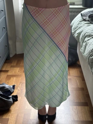 Pastellrutig långkjol i satin - Snygg långkjol med rutigt mönster i pastellfärger som ljusgrön, rosa och blå. Kjolen har en omlottliknande design och är gjord i ett glansigt satinliknande material som faller fint.😚lappen säger st L men den passar perfekt på mig som har st M i byxor 