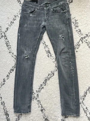 Grå dondup slitna skinny jeans - Snygga grå skinny jeans med slitningar och hål på benen. Jeansen har klassisk femficksdesign och dragkedjor på bakfickorna för en extra cool detalj. Perfekta för dig som gillar en avslappnad och trendig stil.
