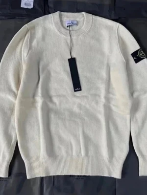 Vit stickad tröja från Stone Island - Snygg vit stickad tröja från Stone Island med rund halsringning och klassisk logotyp-patch på vänster ärm. Tröjan har ribbade muddar vid ärmslut och nederkant, perfekt för en clean och stilren look.