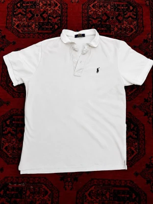 Vit pikétröja från Polo Ralph Lauren - Skick 9/10 utan några defekter, nytvättad och redo att användas! Storlek EU M men passar bättre om man har S då den är 63-64 cm på längden. Liten färgvariation finns beroende på hur tyget fångar ljuset (sista bild) men inget man tänker på. Pris går att diskutera vid bundle köp / snabbaffär 💯