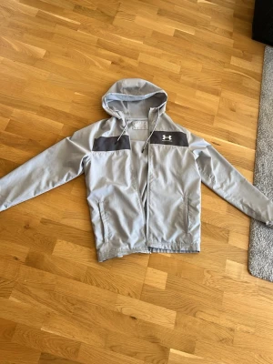 Under Armor Vindjacka - Hej säljer denna snygga under armour vind jackan i size S. Den passar mig bra som är 177 och väger 71kg men kan även passa större och mindre personer. Skicket är 6,5/10. Hyfsat använd men inte någon skada utan bara fläck på bröstet. Går och tvätta bort. Pris går att diskutera vid snabb affär