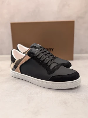 Burberry svart och beige sneakers - Snygga sneakers från Burberry i svart läder och mocka med klassiskt beige rutmönster på sidan. Skorna har svarta skosnören, vit sula och diskret Burberry-logga på tungan och sulan. Perfekta för dig som vill ha en stilren och lyxig look.