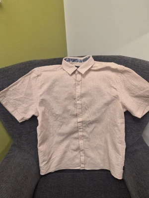 Beige kortärmad skjorta från Indigo Xl - Snygg beige skjorta från Indigo i linne med korta ärmar och klassisk krage. Skjortan har knappar framtill och ett diskret mönstrat tyg på insidan av kragen som ger en extra touch. Perfekt för en avslappnad och stilren look.